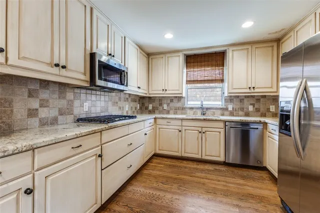 a kitchen with stainless steel appliances granite countertop a refrigerator a sink dishwasher a stove top oven a sink and dishwasher with wooden floor