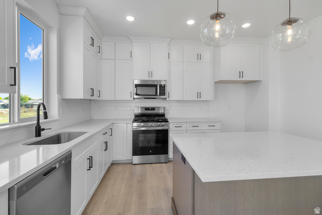 1213 West 500 South Logan, UT 84321 - Photo 7 of 29 Modern kitchen featuring white shaker cabinetry, stainless steel appliances, light-toned wood-finish flooring, a central island with a light-colored countertop, and two contemporary pendant lights