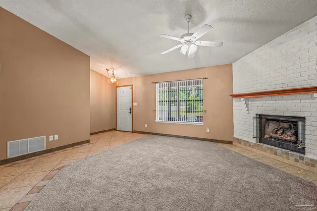 a view of an empty room with chandelier fan and fire place