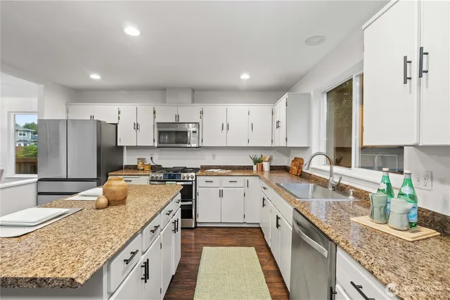 a kitchen with granite countertop kitchen island wooden cabinets a sink dishwasher a stove and a refrigerator