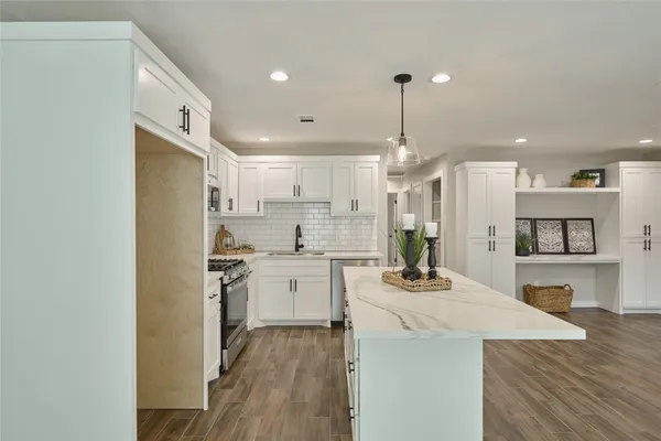 a kitchen with kitchen island a stove a sink a refrigerator and white cabinets with wooden floor