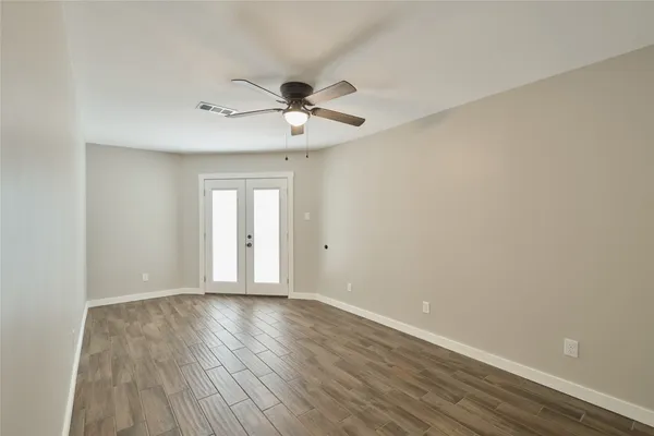 a view of an empty room with wooden floor and a ceiling fan