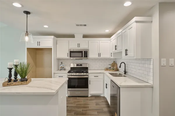 a kitchen with stainless steel appliances a sink a stove a refrigerator a center island and cabinets