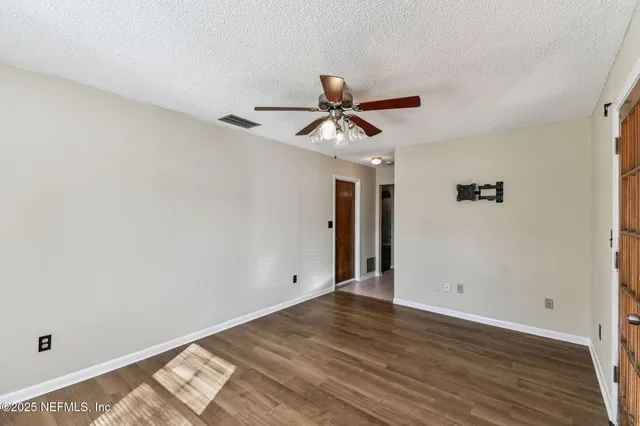 an empty room with wooden floor chandelier fan and windows