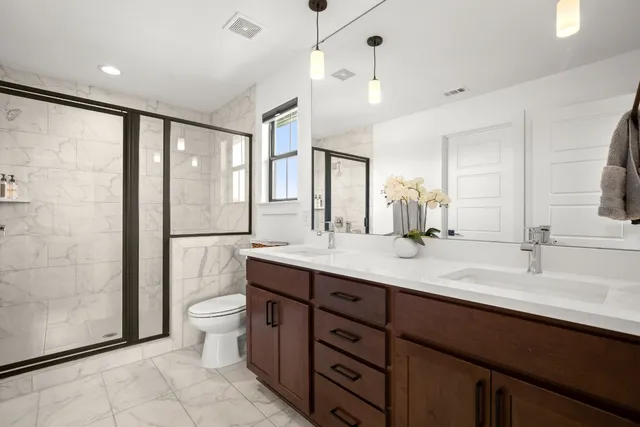 a bathroom with a double vanity sink a toilet a mirror and shower