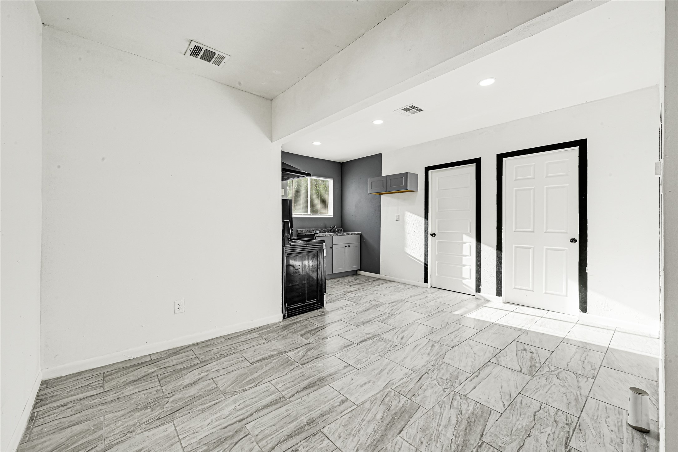 14714 Placid Point Humble, TX 77396 - Photo 5 of 37 This photo showcases a bright, modern kitchen area with sleek tile flooring, recessed lighting, and a neutral color palette. The space includes a small window for natural light, black and gray cabinetry, and two contrasting doors, adding a contemporary touch.