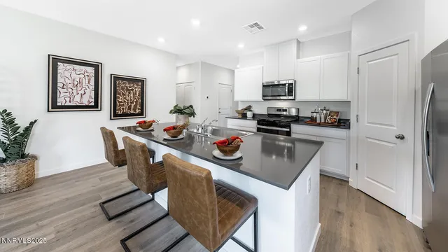 a kitchen with stainless steel appliances granite countertop a refrigerator a stove top oven a sink dishwasher and white cabinets with wooden floor