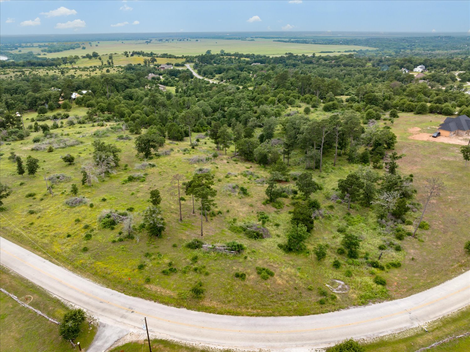 0 McAllister Road Bastrop, TX 78602 - Photo 8 of 12 Vast, verdant landscape with scattered trees, a paved road, and glimpses of distant structures.
