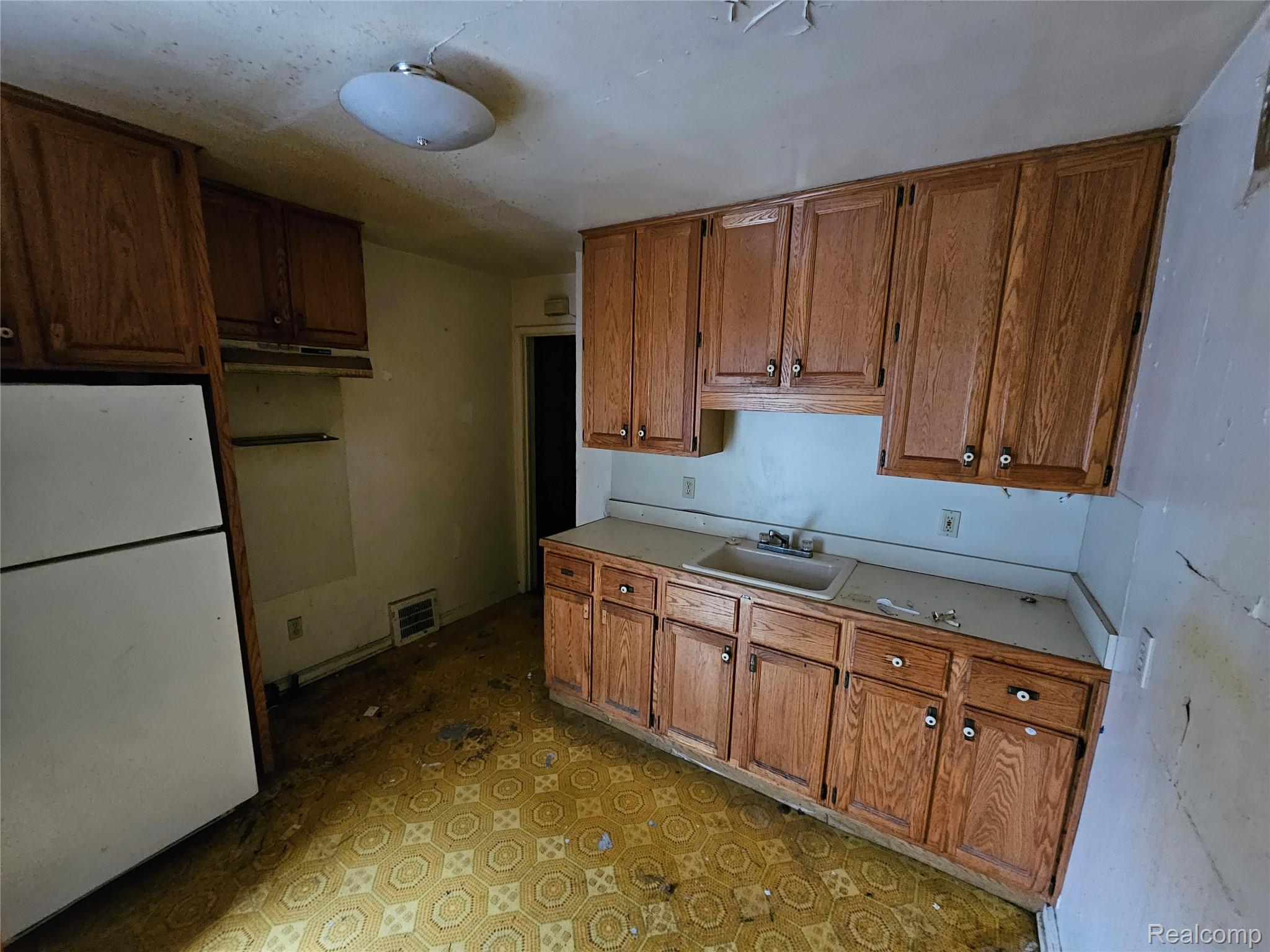 19442 Moross Road Detroit, MI 48224 - Photo 29 of 48 Kitchen featuring freestanding refrigerator, light floors, light countertops, brown cabinets, and under cabinet range hood