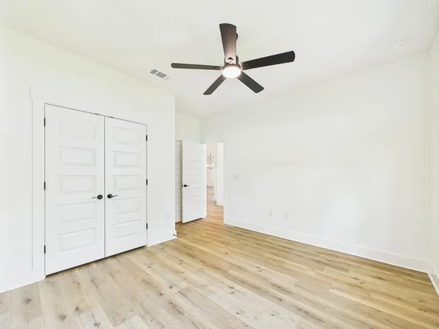 an empty room with wooden floor fan and windows