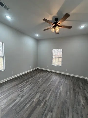 an empty room with wooden floor a ceiling fan and windows