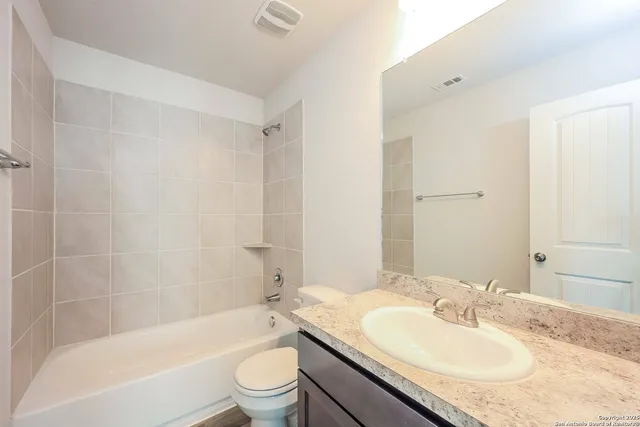a bathroom with a granite countertop bathtub shower sink vanity mirror and toilet