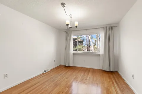 an empty room with wooden floor chandelier and windows