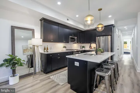 a living room with stainless steel appliances kitchen island granite countertop a refrigerator a sink dishwasher and a dining table with wooden floor