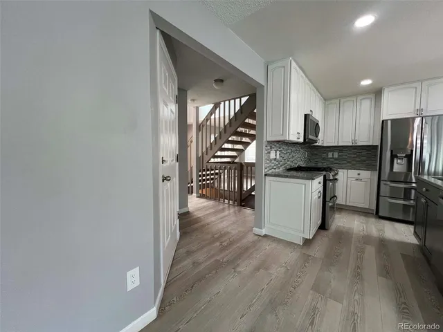 a kitchen with stainless steel appliances granite countertop a stove top oven a refrigerator a sink and dishwasher with wooden floor