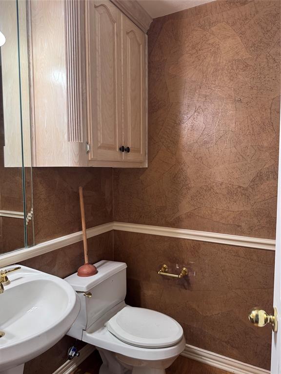 1704 South Bowen Road Pantego, TX 76013 - Photo 4 of 37 Half bath off of entry way. Pedestal sink with brass-finish faucet, white toilet, and textured wall finish