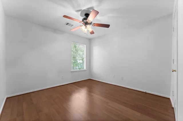 an empty room with wooden floor fan and windows