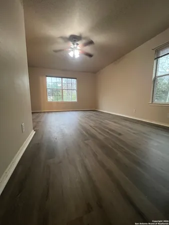 an empty room with wooden floor chandelier fan and windows