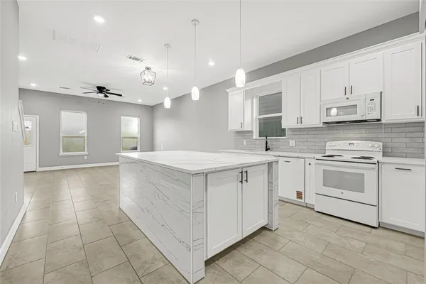 a kitchen with kitchen island granite countertop white cabinets a sink a stove a oven and a window