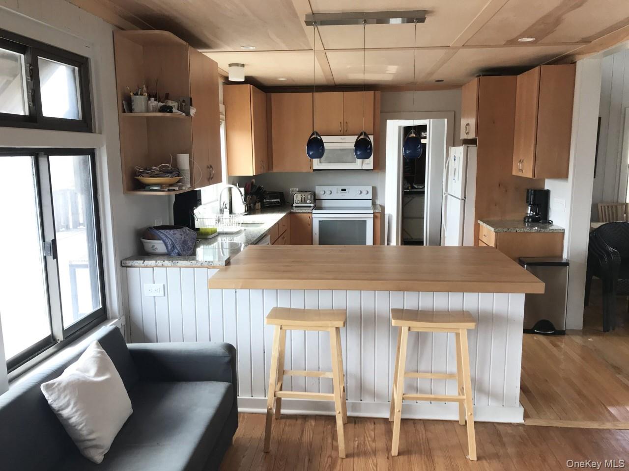 35 Sloop Walk Ocean Beach, NY 11770 - Photo 5 of 21 Kitchen featuring a peninsula, white appliances, light wood-type flooring, a kitchen breakfast bar, and pendant lighting