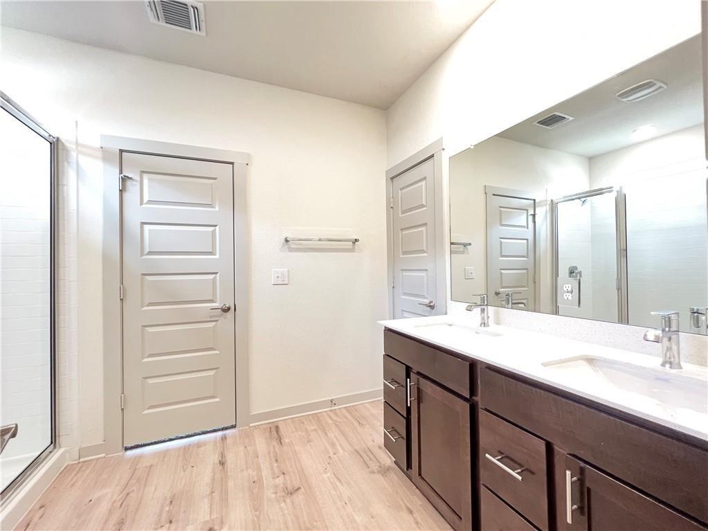 10600 Defender Trail Austin, TX 78754 - Photo 8 of 21 Bathroom featuring a stall shower, double vanity, and light wood-type flooring