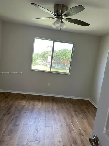 an empty room with wooden floor fan and windows