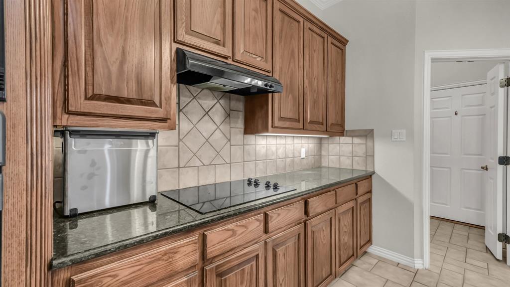 203 Mockingbird Lane Aledo, TX 76008 - Photo 18 of 37 Kitchen featuring wood cabinetry, dark countertops, tile backsplash, and a black cooktop with an overhead exhaust fan