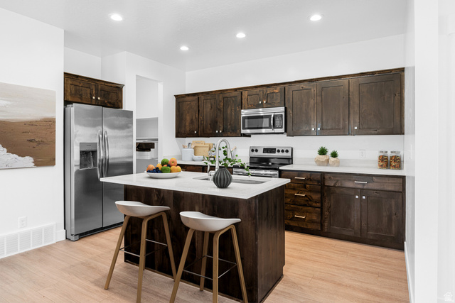 1503 South Deerbrook Road, Unit 348 Santaquin, UT 84655 - Photo 2 of 14 Kitchen with dark wood finish cabinetry, a center island with sink, stainless steel appliances, light wood-style flooring, and a breakfast bar