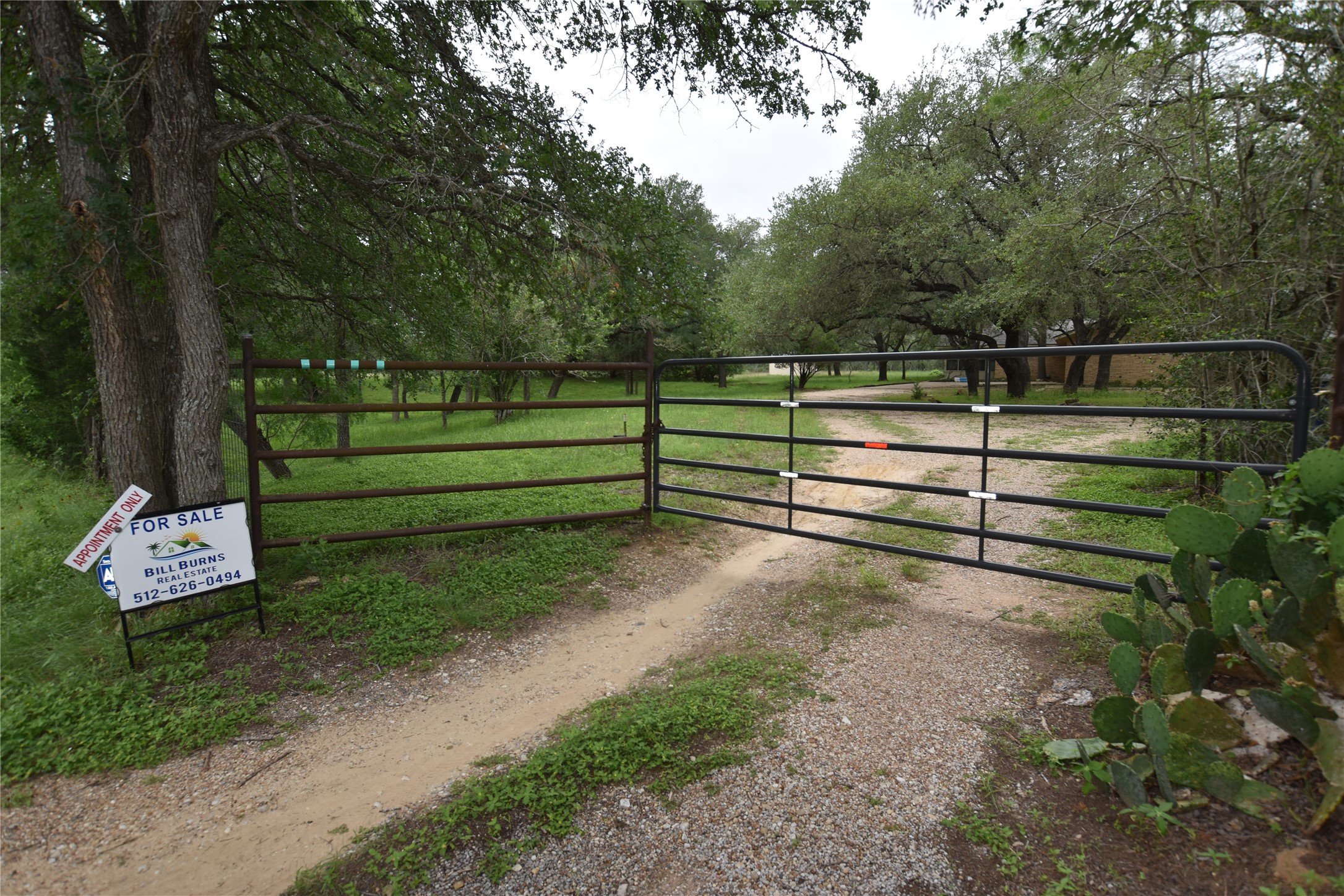 687 Fm 812 Road Red Rock, TX 78662 - Photo 6 of 40 Gated Gravel drive entryway featuring a metal gate, mature trees, and natural vegetation