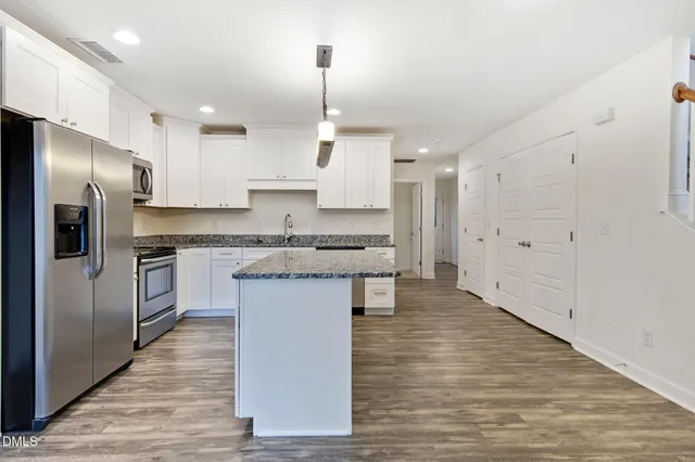 a kitchen with kitchen island granite countertop a refrigerator a oven a stove and white cabinets with wooden floor