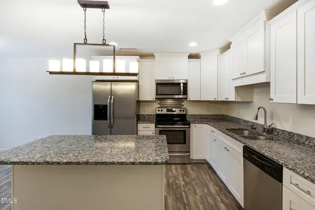 a kitchen with kitchen island granite countertop stainless steel appliances a sink refrigerator and cabinets
