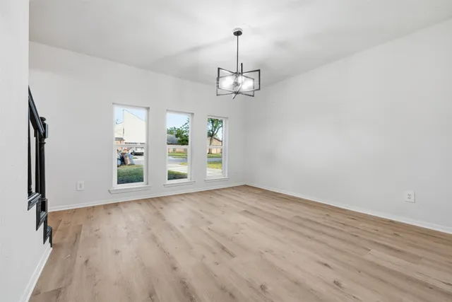 an empty room with wooden floor chandelier and windows