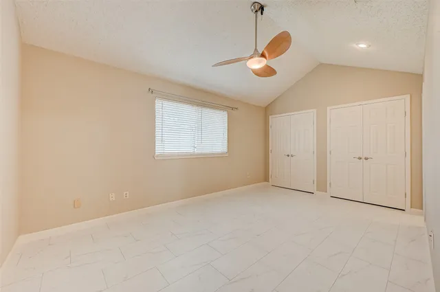an empty room with chandelier fan and windows