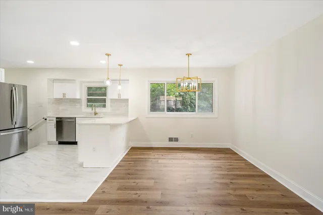 an empty room with wooden floor kitchen view and a window