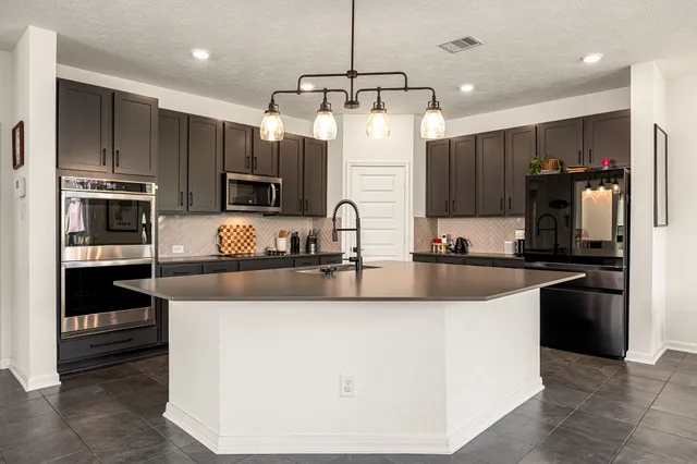 a large kitchen with kitchen island a large counter top stainless steel appliances and cabinets