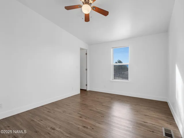 an empty room with wooden floor chandelier fan and windows