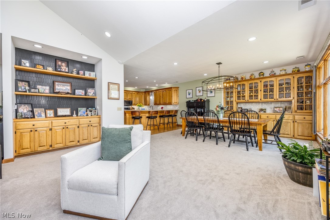 1602 Glendale Road, Unit 3 Marietta, OH 45750 - Photo 10 of 49 Open-concept interior featuring light-toned carpeting, recessed lighting, built-in shelving with black hexagonal tile backing, a dining area with a linear chandelier, and extensive built-in cabinetry with glass-front uppers