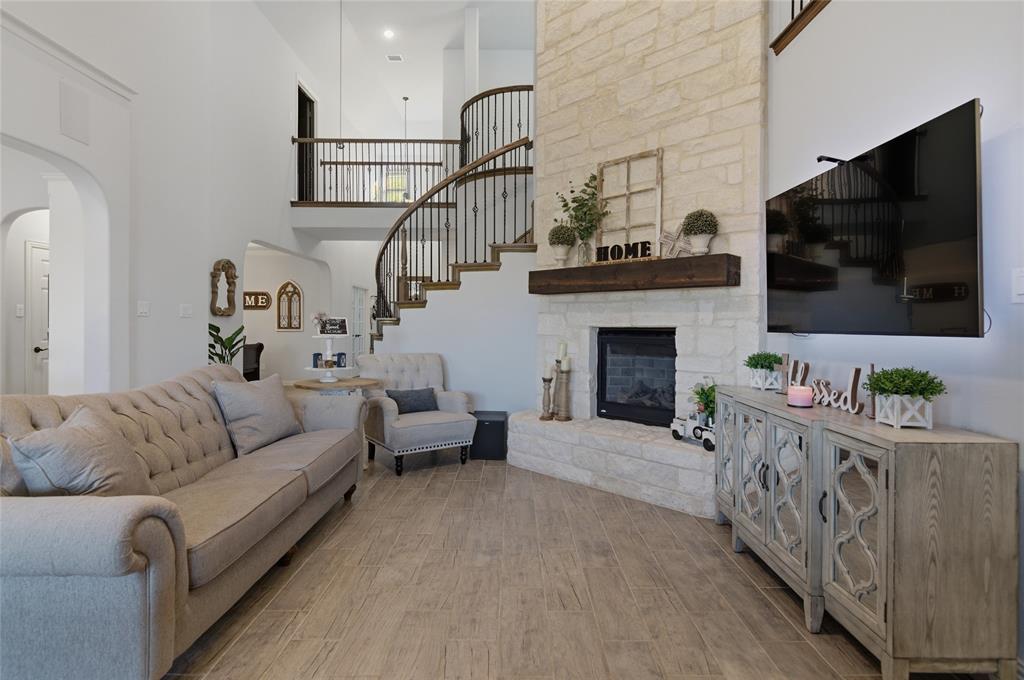 464 LeTara Ranch Drive Haslet, TX 76052 - Photo 8 of 37 Two-story living area featuring wood-finish flooring, a stone-clad fireplace with a dark wood mantel, and a prominent curved staircase with dark wood handrails and black metal balusters