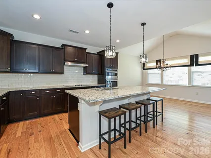 a kitchen with stainless steel appliances kitchen island granite countertop a table chairs sink and cabinets