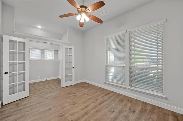 an empty room with wooden floor chandelier fan and windows