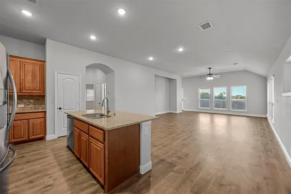 a kitchen with stainless steel appliances granite countertop a stove top oven a sink dishwasher a refrigerator and a dining table with wooden floor
