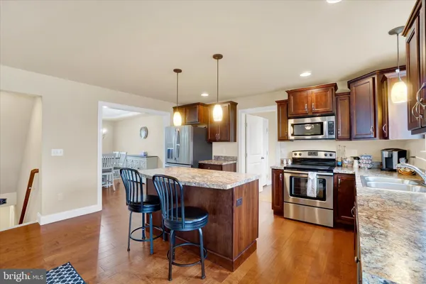 a kitchen with stainless steel appliances granite countertop a stove a refrigerator a kitchen island a dining table and chairs with wooden floor
