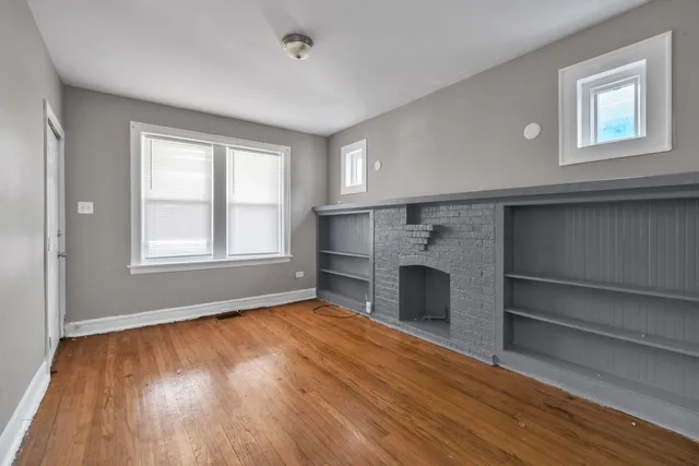 a view of an empty room with wooden floor fireplace and a window