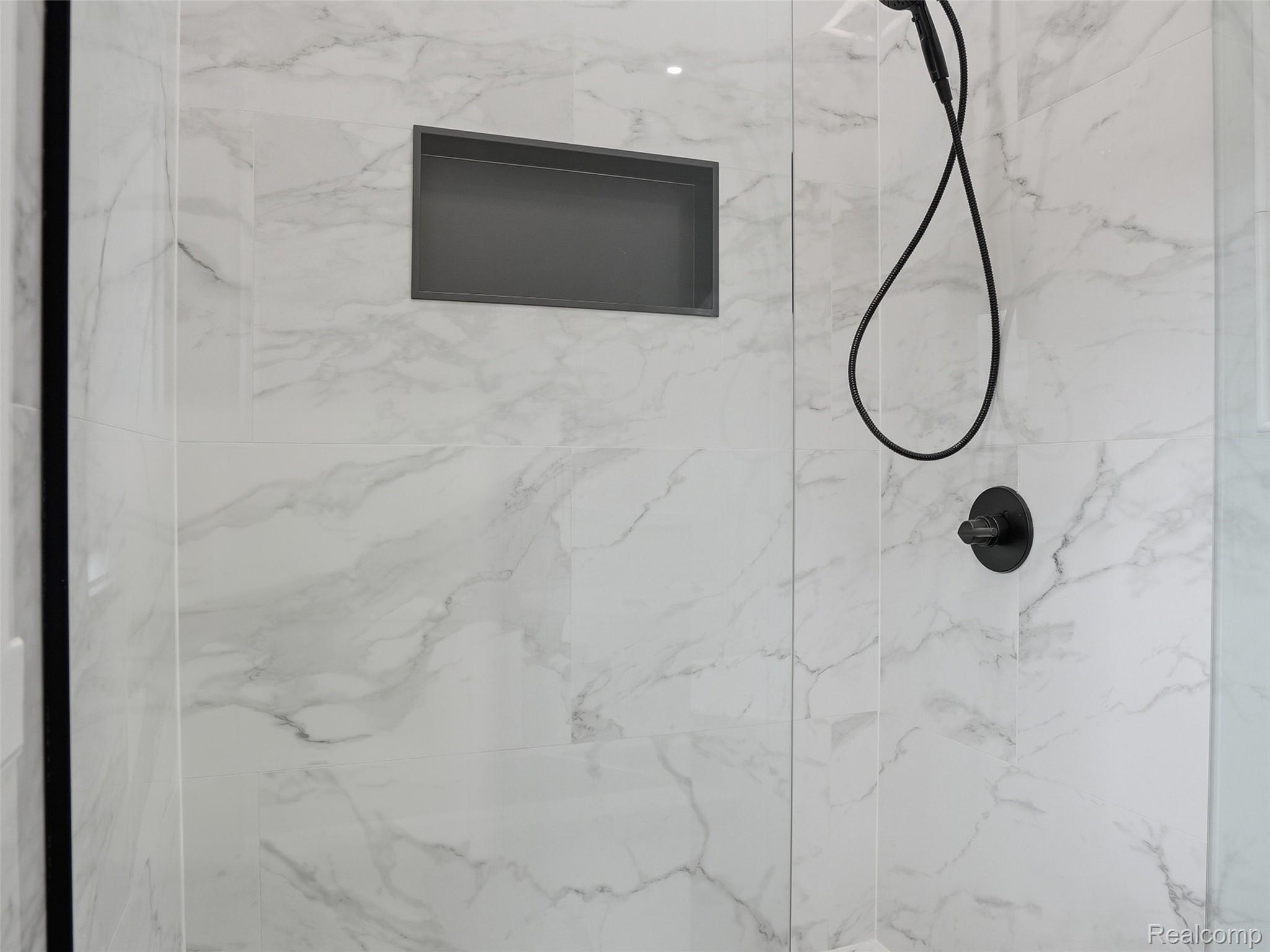 77850 Angling Road Richmond, MI 48062 - Photo 41 of 54 Shower enclosure featuring marble-look wall tiling, a matte black handheld shower fixture, a circular matte black control knob, and a recessed shower niche