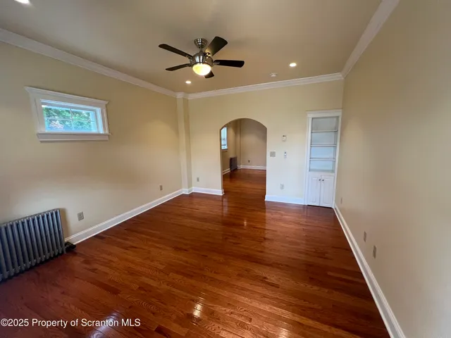 a view of an empty room with wooden floor and a ceiling fan