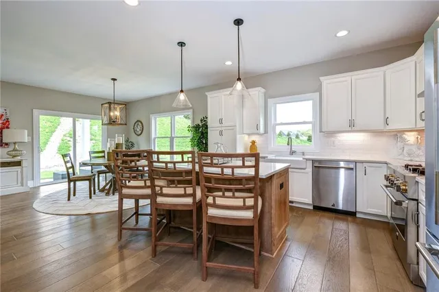 a kitchen with stainless steel appliances granite countertop a stove a refrigerator a kitchen island a dining table and chairs with wooden floor