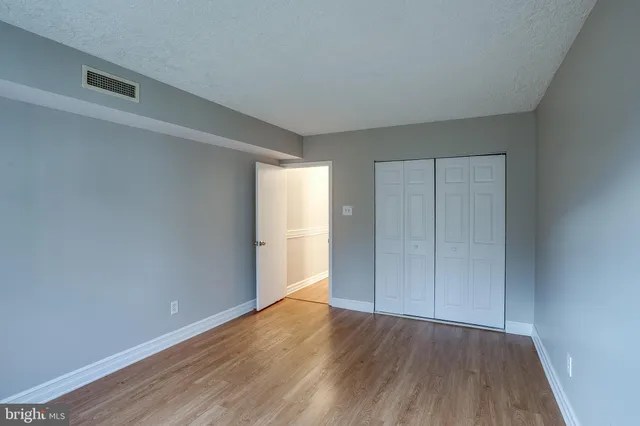 a view of an empty room with wooden floor and closet