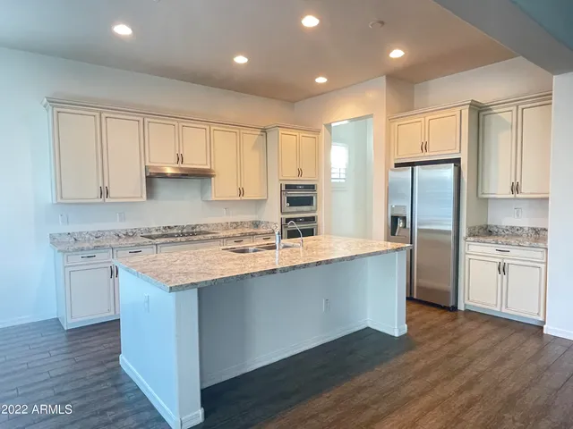 a kitchen with stainless steel appliances granite countertop a refrigerator a sink dishwasher a stove and white countertops with wooden floor