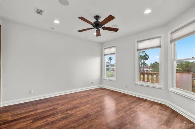 an empty room with wooden floor windows and fan