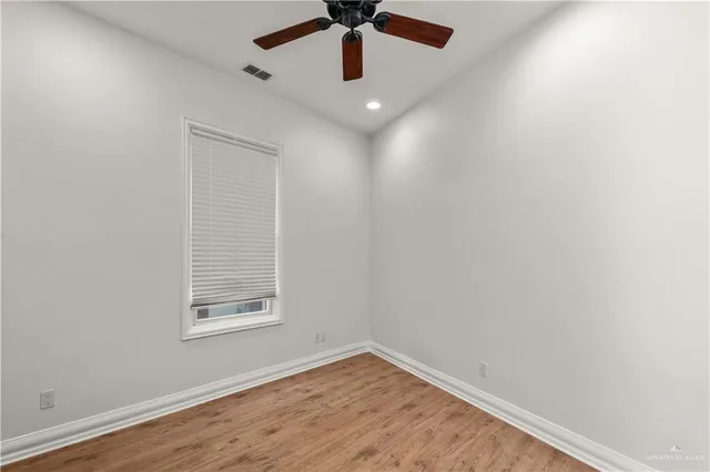 an empty room with wooden floor ceiling fan and windows